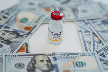 conceptual vial of coronavirus or covid-19 vaccine shown surrounded by US one hundred dollar bills