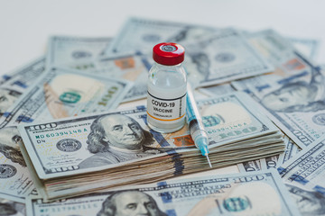 Fototapeta premium conceptual vial of coronavirus or covid-19 vaccine on a stack of US one hundred dollar bills next to a syringe and more banknotes