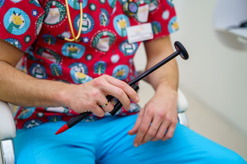 Crop view of doctor with reflex black hummer in hands. Pediatric concept. Doctor in bright scrubs.