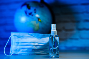 Sanitizer or antiseptic on earth globe behind the mask bakground. Save the planet. Fight the pandemic spreading. COVID-19 and coronavirus