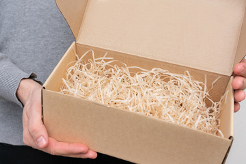 Man shows an open gift box with decorative straw or shavings, men's hands, closeup, copy space