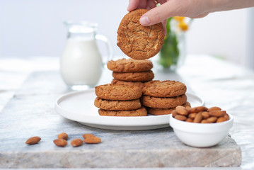 Hand with tasty oatmeal almond cookies with jar of milk on the old marble table beautiful close-up on white background