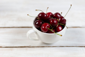 Cup with ripe red cherries on a white wooden rustic background
