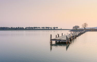 Fototapeta premium Early morning. Smooth surface of the lake and the old wooden bridge destroyed Place for relaxation and meditation. Place for fishing.