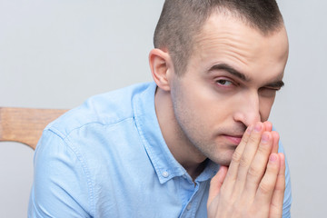 Sly young man prays sitting down, portrait, closeup