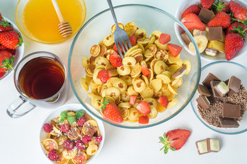 mini pancake cereal bowl with fresh strawberries banana chocolate, coconut shavings and honey in small plates. the view from the top . the trend of self-isolation