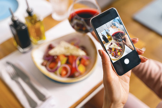 Young woman taking picture of food and wine with cellphone