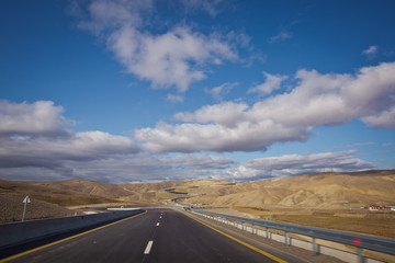 Asphalt road and bright blue sky with fluffy clouds . Empty desert asphalt road from low angle with mountains and clouds on background. road, red desert landscape . Open road with blue clouds .