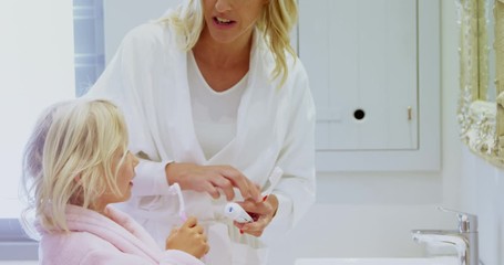 Mother teaching her daughter to brush her teeth in bathroom at home