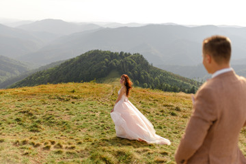 Bride and groom during a wedding photo shoot in the mountains. The bride stands away from the groom and looks at her beloved.