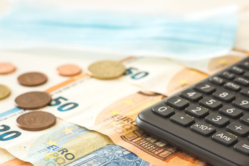Euro bills and coins next to a calculator and a face mask, as a symbol of the economic crisis caused by the covid19. Coronavirus, concepts, financial crisis
