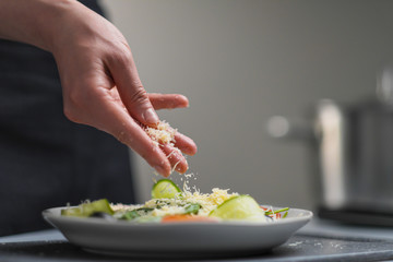A female chef in a white uniform and a black apron in the restaurant kitchen. Cooking. The cook sprinkles grated cheese prepared food.