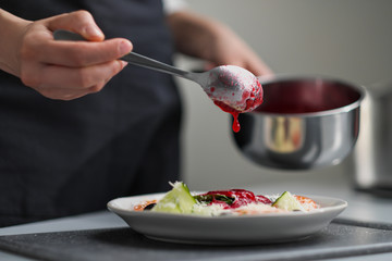 A female chef in a white uniform and a black apron in the restaurant kitchen. The cook pours red cranberry salad sauce. Making and decorating food.