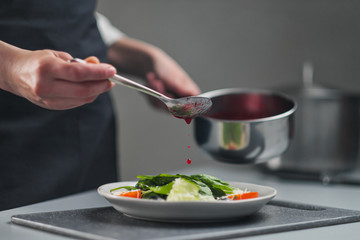 A female chef in a white uniform and a black apron in the restaurant kitchen. The cook pours red cranberry salad sauce. Making and decorating food.
