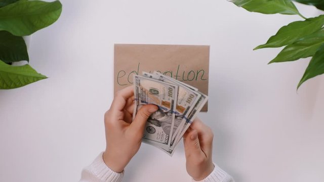 Top down view. Female hands count american money, dollars, and then put it on an envelope with an inscription, the word Education. The girl is saving money for education.