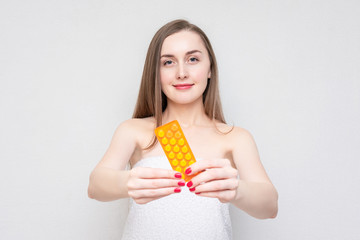 Woman in towel with the yellow pills in her hand, white background. Concept of birth control pills