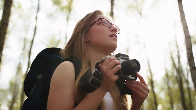 Caucasian smiling woman with vintage camera enjoying holiday in the nature. Backpacker in the forest. Lens flare.