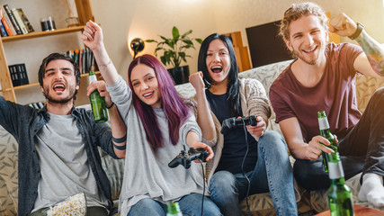 Group of multi ethnic young friendsplaying in video games at home while drinking beer