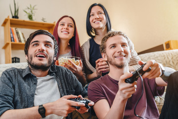 Multiethnic joyful group of young people playing games on console while having party at home
