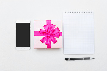 Notebook, gift with pink ribbon 8 March, white smartphone, white background, copy space, top view