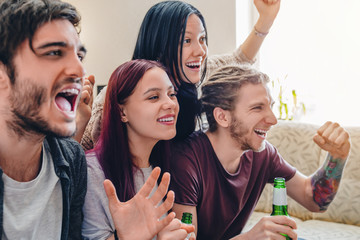 Group of young friends enjoying great football game and drinking beer at home