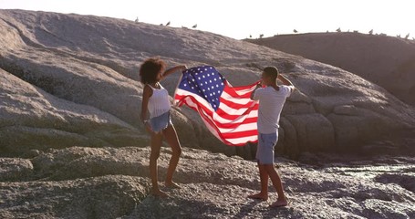 Couple holding American flag on rock at beach in the sunshine - Powered by Adobe