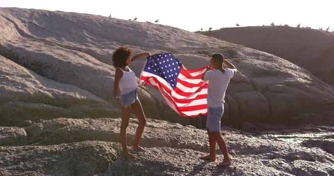 Couple holding American flag on rock at beach in the sunshine