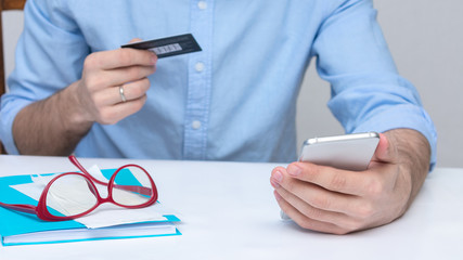 Man with plastic card and phone, guy paying bills via a smartphone, man's hands, cropped image, closeup, 16:9