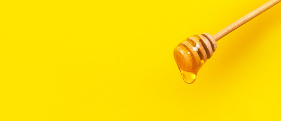 Honey dripping from honey dipper on yellow background. Thick honey dipping from the wooden honey spoon. Healthy food and diet concept