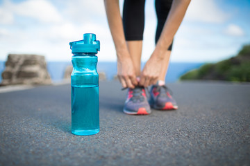 Drink water, and active lifestyle. Runner tying shoe next to bottle of water.