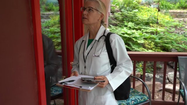 Making a rural house call, a closeup of a mature woman doctor or nurse walks to the door, knocks, smiles and shows ID badge.