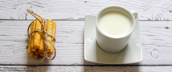 Cup of milk and breadstick on a wooden background. Healthy breakfast.