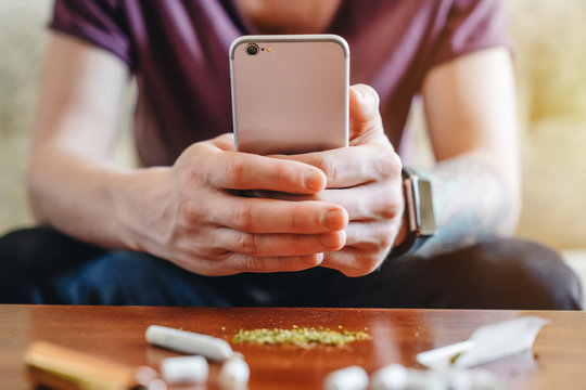 Young man making photo on his mobile phone of his joint and weed