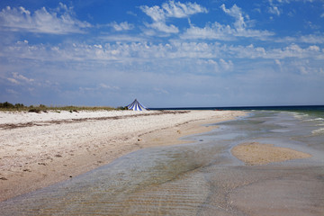 Striped marquee on sand beach, sea and blue cloudy sky at summer