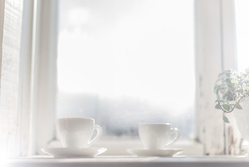 Two white cups with coffee stand on a white window on a blurred background. morning.