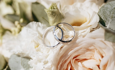 Two wedding rings lie on a bouquet for the bride in nature under the bright sun in the summer. Wedding bouquet of flowers in pastel shades, roses. Silver or white gold.