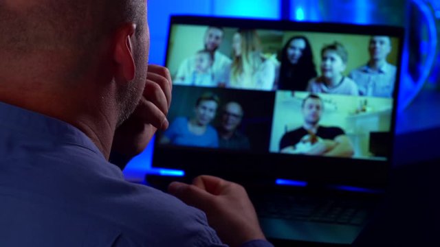 Over the shoulder close-up view of an adult balding man video call relatives talking webcam conference chat app on the laptop screen on the table. The concept of a family video call.