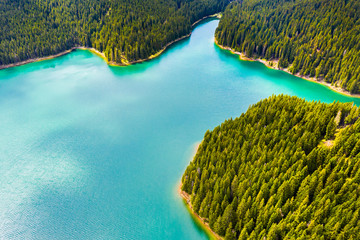Turquoise water in a mountain forest lake with pine trees. Aerial view of blue lake and green forests. View on the lake between mountain forest. Over crystal clear mountain lake water. Fresh water