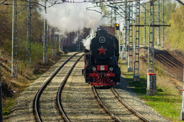 Black locomotive with red star moves, rides on the railway tracks. The curve of the railway tracks, warm Sunny spring day of may 9. Paths paved with gravel