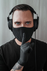 man in a black mask put finger to lips. in headphones. hush sign. keep silence. listening music. 