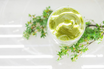 Dalgona matcha coffee or tea - green iced coffee drink with milk on white table with plants, sunny light. New trend drink in social media. Morning healthy reverse latte. Selective focus, copy space.