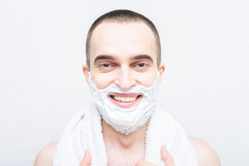 Smiling guy with shaving foam on his face, looks at the camera, white background