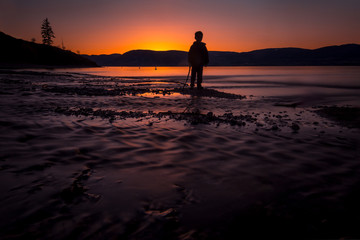 Silhouetted Boy During Sunset By The Shore With Flowing Water