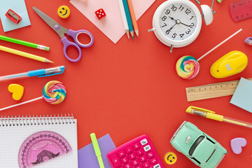 back to school concept. Colorful school accessoties . On coral background are alarm clock, calculator, pencils, pens, candies, toys, and other supplies. Top view, flat lay, space for text . 