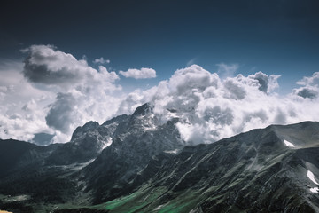 Clouds covered the top of the mountain with glaciers on a sunny day against the sky. Monument of nature of UNESCO, Adygea, Fisht, favorable ecology. The famous tourist route.