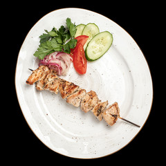 chicken skewer with vegetables tomatoes and cucumber slices on a white plate top photo, isolate, black background