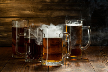 light beer with foam in mugs with smoke in a bar on a wooden table