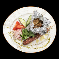 Lula kebab on a skewer with vegetables tomatoes and cucumber slices on a white plate top photo, isolate, black background