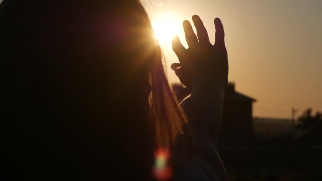 close-up of a woman's hand in silhouette touching the sun rays in a field