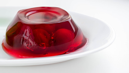 White plate with cherry berries in red jelly on a white background.